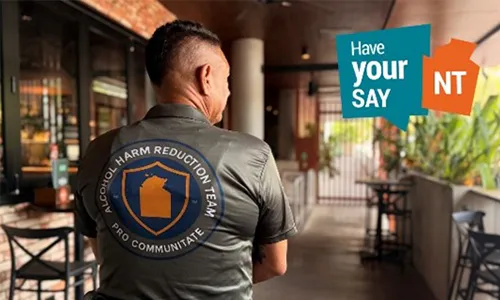 Person in an Alcohol Harm Reduction Team shirt with a “Have Your Say NT” graphic.
