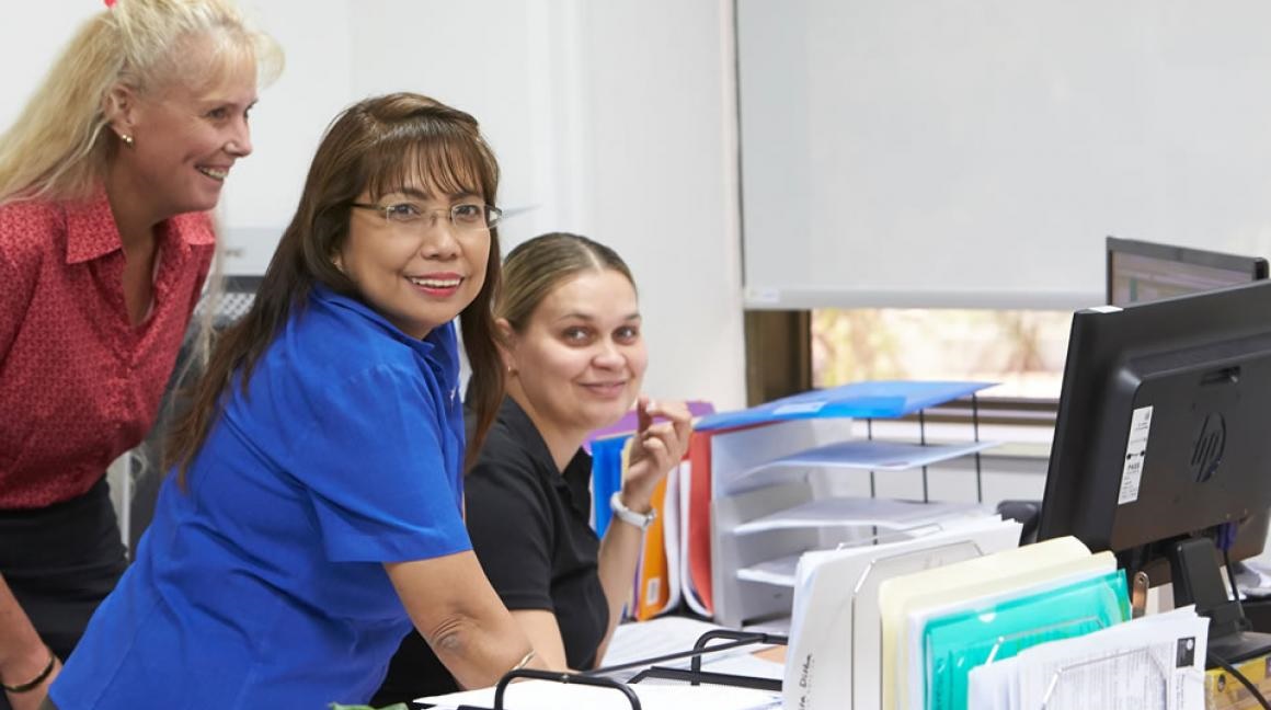 Three women at a desk viewing a computer