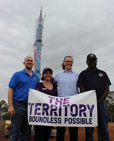 Group of people standing in front of rocker with The Territory banner